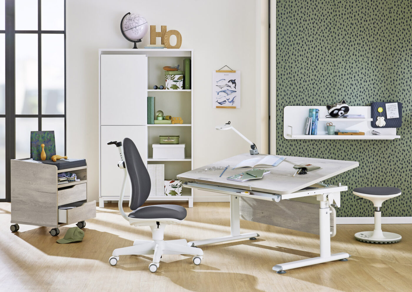 Modern eingerichtetes Kinderzimmer mit PAIDI Kinderschreibtisch Diego, grauem Schreibtischstuhl Jooki und Sitzhocker Speedy vor einer grünen Akzentwand.